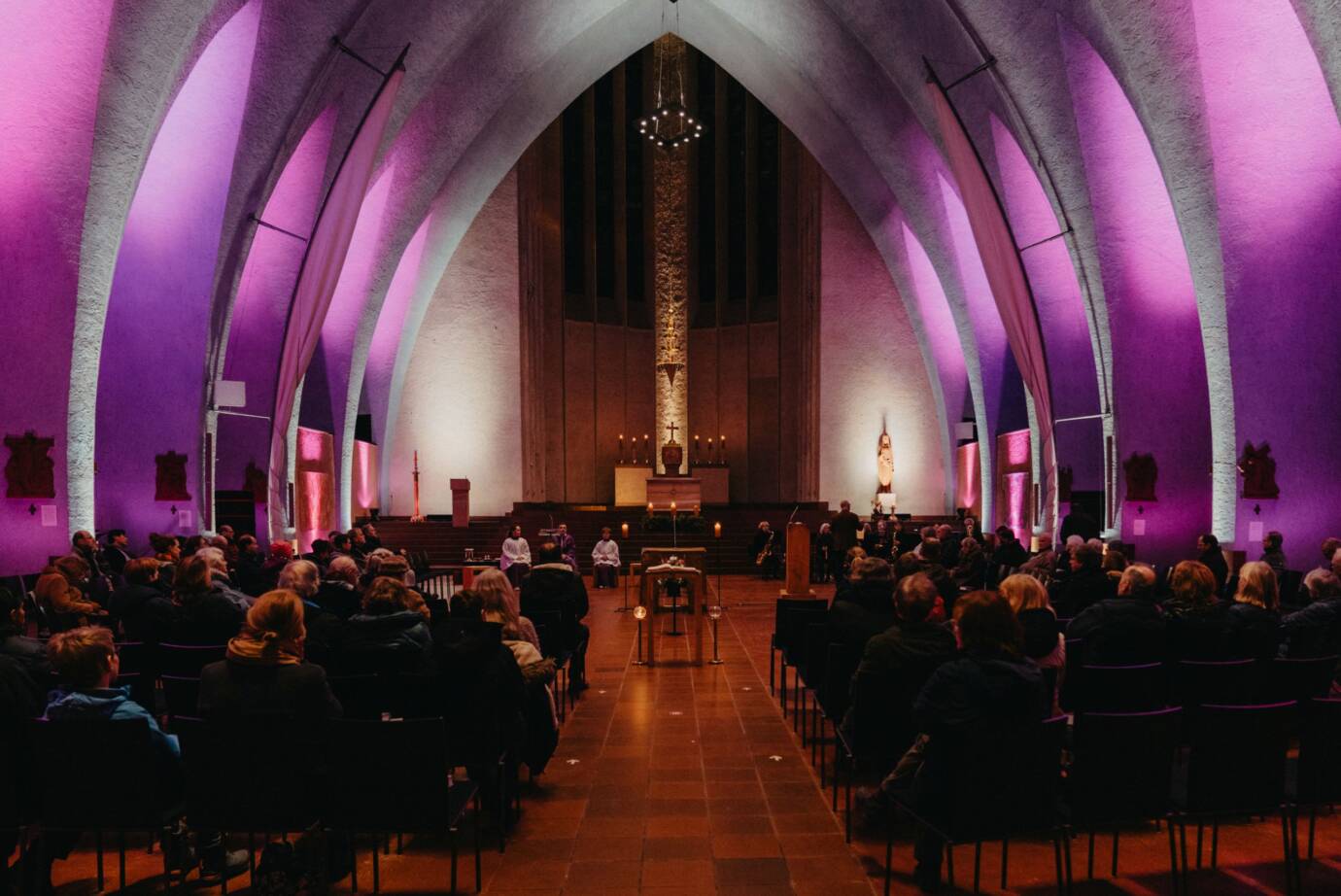 Kircheninnenraum mit lila Licht und Gottesdienstbesuchern