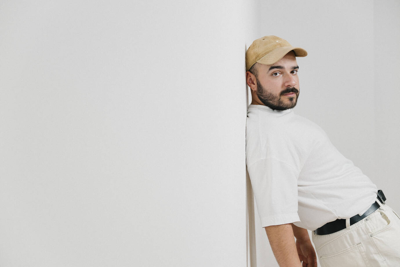 Mann mit Kappe lehnt an weißer Wand